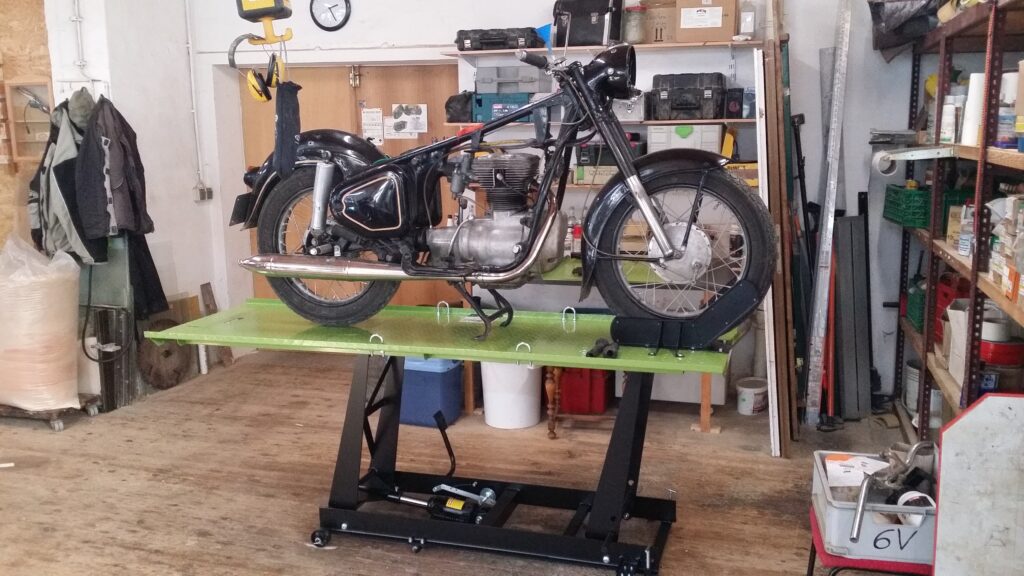 Eine AWO Sport steht teilzerlegt auf einer Hebebühne in einer Werkstatt.